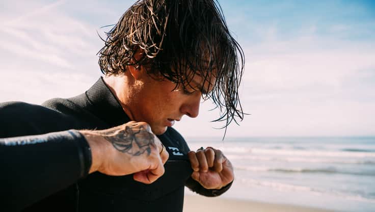 Surfer zieht sich seinen Chest Zip Neoprenanzug an
