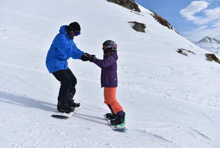 Snowboardlehrer hilft dem Schüler bei den ersten Rutschübungen