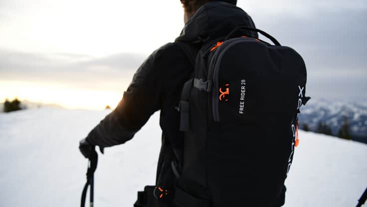 Two avalanche compatible rucksacks outside, with two riders and a tent