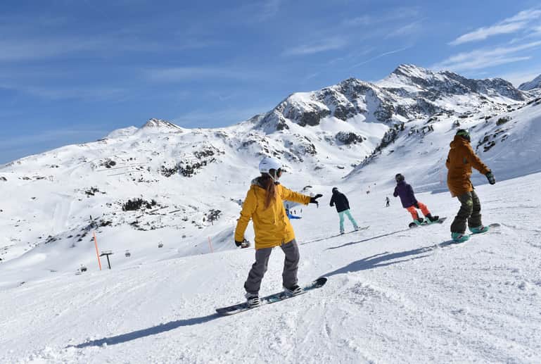 Snowboardschüler fahren hinter einander auf der Piste