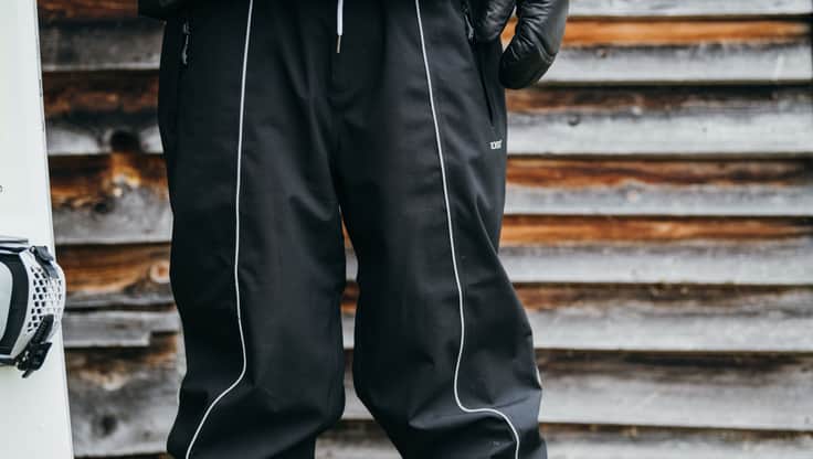 A snowboarder standing in snow in bib-pants