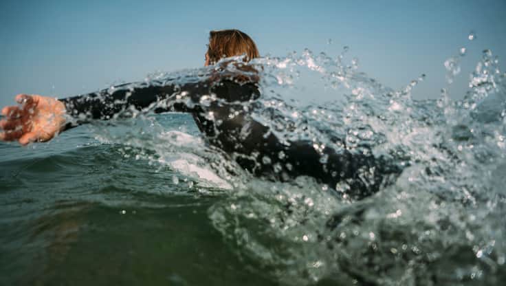 Ein Surfer sitzt auf seinem Longboard im Meer